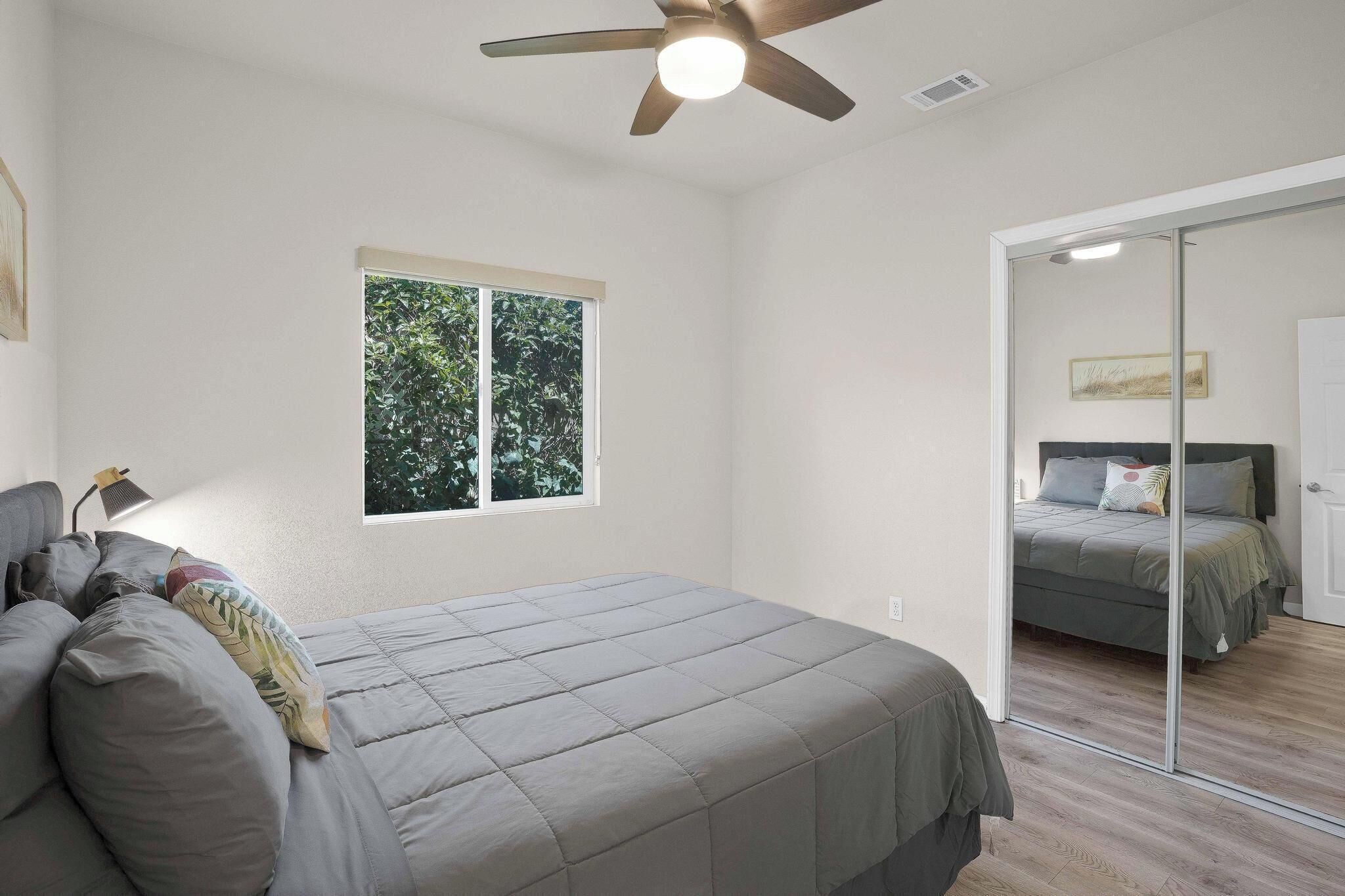 Ein Schlafzimmer mit einem Bett, einem Deckenventilator, einem Fenster und einem Spiegel.