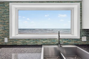 A bathroom with a large window overlooking a beach, a modern sink, and a tiled backsplash.