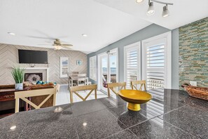 A modern kitchen with a marble countertop, a ceiling fan, and a view of the ocean through large windows.