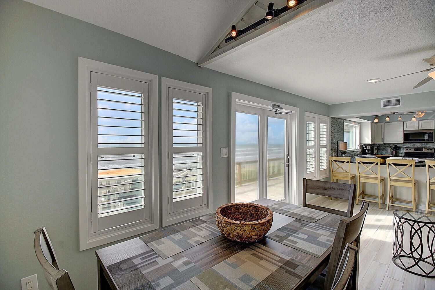 A spacious kitchen with modern appliances, a dining area with a large table, and a view of the ocean through large sliding doors.