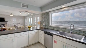 Una cocina moderna con armarios blancos, encimera negra y un amplio ventanal con vistas al océano.