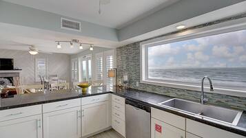 A modern kitchen with white cabinets, a black countertop, and a large window overlooking the ocean.