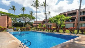 A swimming pool with clear blue water, surrounded by palm trees and a building with multiple balconies.