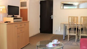 A compact living space with a wooden cabinet, a television, a glass coffee table with cups, and a dining area with chairs and a table. - Charming Studio in Vars, 30m from Slopes, Sleeps 4 (Vars)