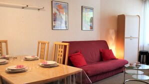 A dining area with a wooden table set for four, a red sofa, and a glass coffee table. - Charming Studio in Vars, 30m from Slopes, Sleeps 4 (Vars)