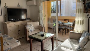 A living room with a sofa, a glass-top coffee table, a television, and a dining area with a table and chairs. - Central apartment near beach in Banyuls-sur-Mer (Banyuls-sur-Mer)
