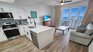 Une cuisine moderne dotée d’un îlot central, un coin repas avec une table en bois et un salon avec un canapé gris.