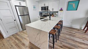 Une cuisine moderne dotée d’un îlot en marbre, d’appareils électroménagers en acier inoxydable et de tabourets de bar en bois.