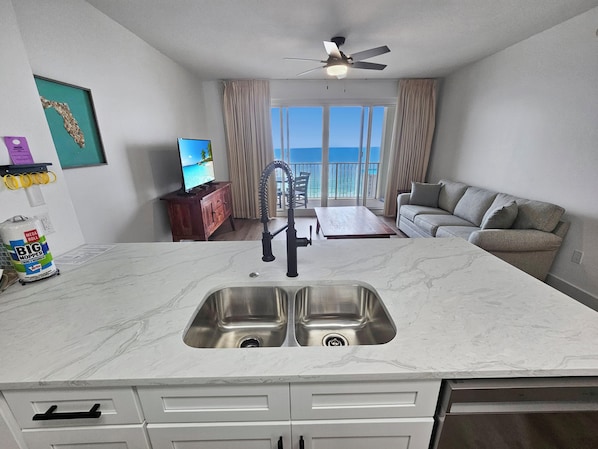 A modern kitchen with a large island, a double sink, and a dining area with a view of the ocean.