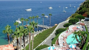 A coastal hotel with a pool area, palm trees, and boats in the background. - H230: Comfortable 2BD Villa w/ Ocean Views, WIFI, 4-seat Golf Cart (Avalon)