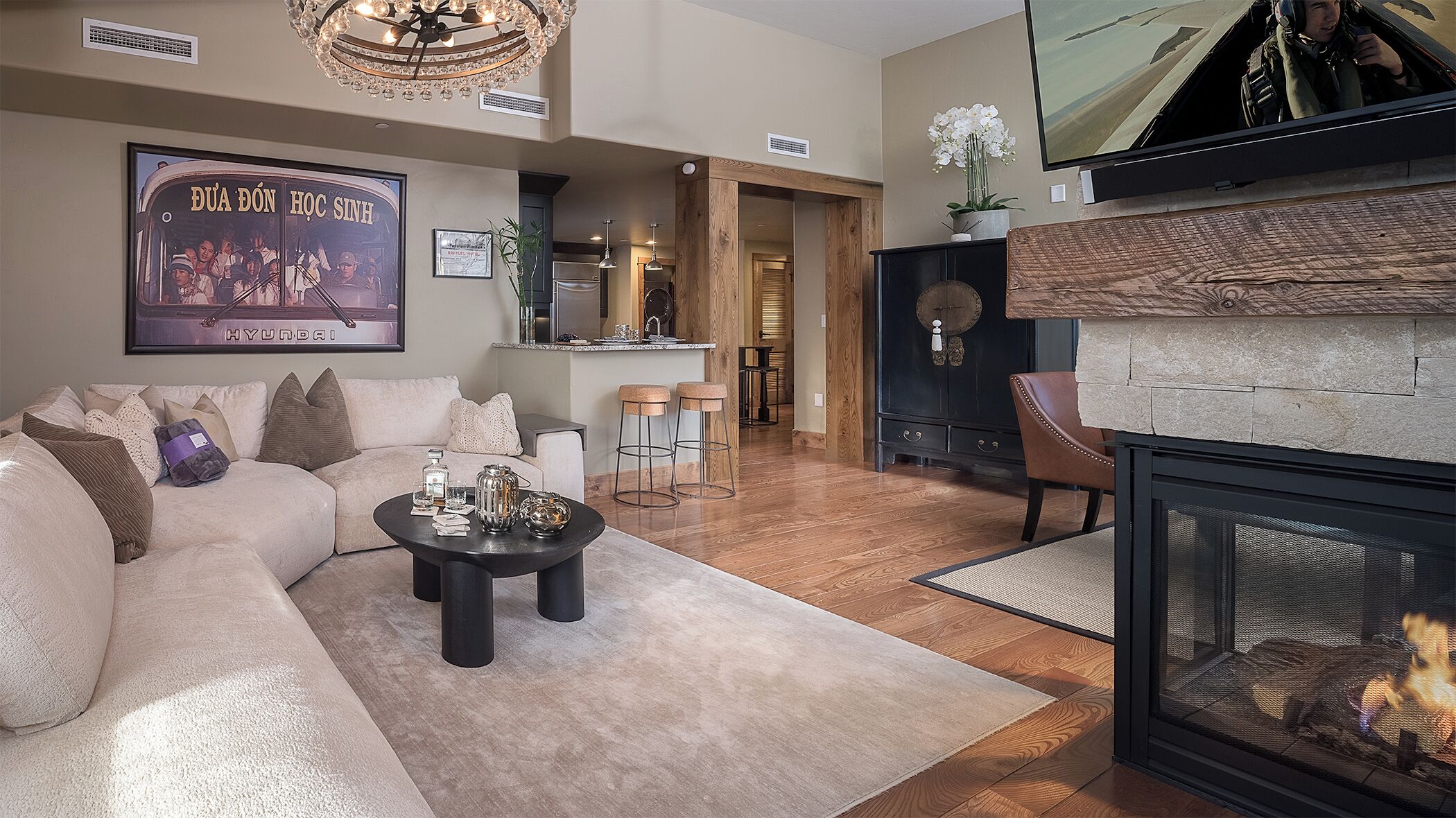 A modern living room with a sofa, coffee table, and fireplace. There is a kitchen area in the background and a television mounted on the wall.