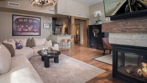 Un salon moderne avec un canapé, une table basse et une cheminée. On aperçoit un coin cuisine au fond et un téléviseur fixé au mur.
