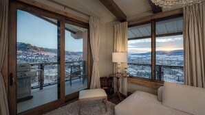 Une pièce dotée d’une grande fenêtre donnant sur un paysage enneigé, d’un plafond en bois et d’une petite table avec une lampe.