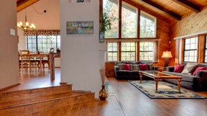 A spacious living room with a wooden ceiling, large windows, a sofa, and a dining area with wooden furniture.