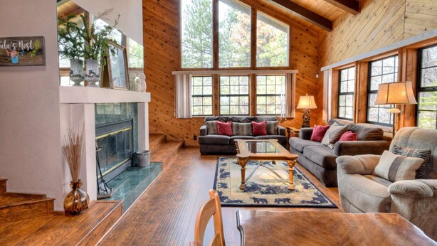 A cozy living room with a fireplace, large windows, and wooden floors.