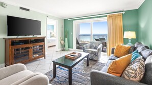 A living room with a flat-screen TV, a wooden entertainment unit, a sofa, and a coffee table. There is a balcony with a view of the ocean. - 🌊 Views That Go On Forever (Destin)