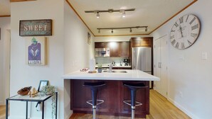 A modern kitchen with a central island, stainless steel appliances, and a large wall clock.