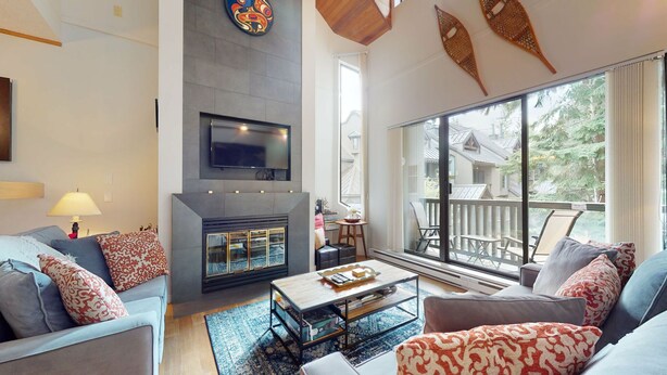 A modern living room with a fireplace, comfortable seating, and large windows offering a view of the outdoors.
