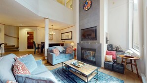 A spacious living room with a fireplace, a dining area, and a staircase leading to an upper level.