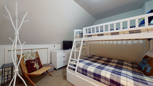 Habitación con literas, una escalera, una silla con un cojín de ciervo, un escritorio blanco pequeño y una ventana.
