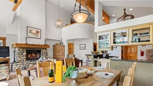 A spacious living area with a stone fireplace, wooden dining table, and modern kitchen cabinetry.