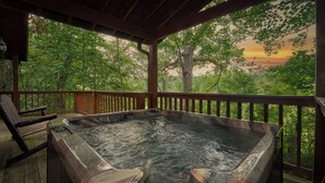 Ein Whirlpool auf einer Holzterrasse mit Blick auf einen Wald und einen Sonnenuntergang.