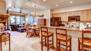 A spacious kitchen with wooden cabinets, a central island with bar stools, and a dining area with a sofa and chairs. - Tl2212 Stunning Condo with Private Balcony Overlooking the Pool (Steamboat Springs)