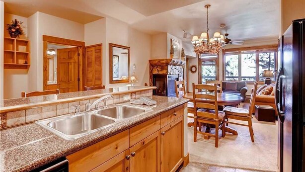 A kitchen with wooden cabinets, granite countertops, a double sink, and a dining area with a table and chairs. - Tl2212 Stunning Condo with Private Balcony Overlooking the Pool (Steamboat Springs)