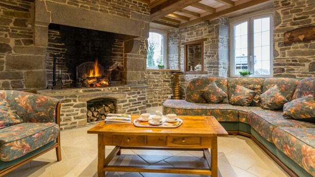 Ein gemütliches Wohnzimmer mit Kamin aus Stein, Holzbalken und einem grünen Sofa.