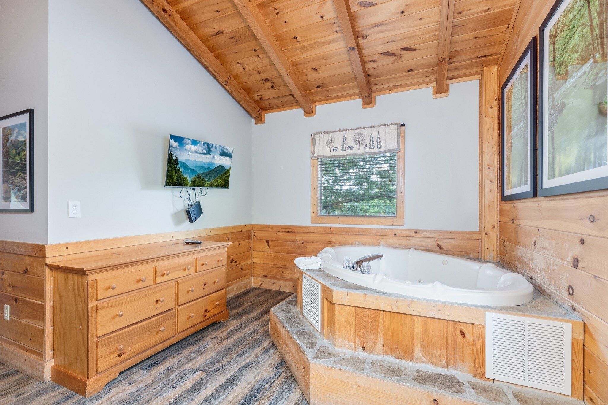 A wooden cabin bathroom with a wooden vanity, a large bathtub, and framed pictures on the walls.