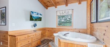 A wooden cabin bathroom with a wooden vanity, a large bathtub, and framed pictures on the walls.