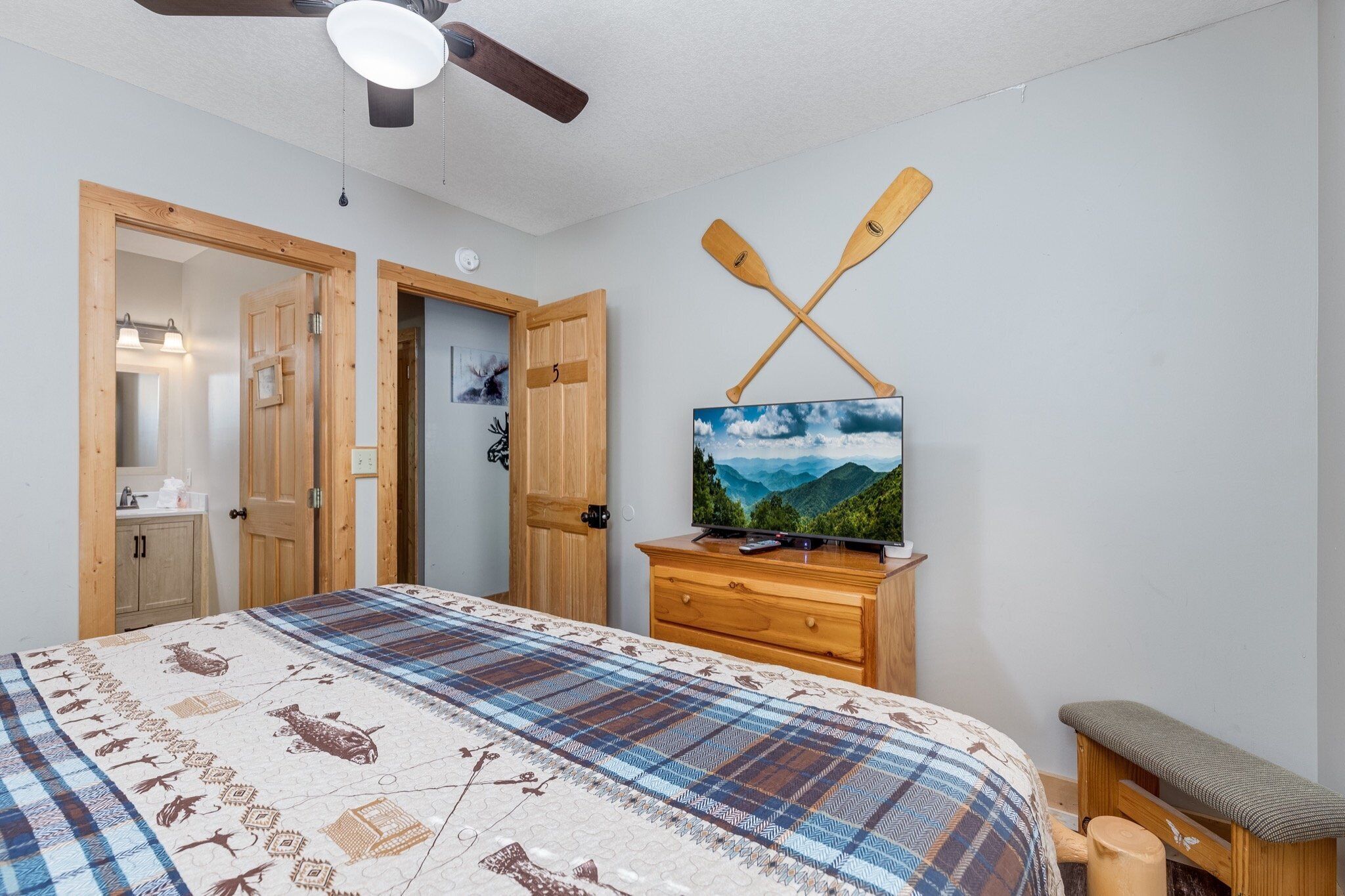 Une chambre à coucher avec un lit, une commode en bois, une télévision et un ventilateur de plafond.