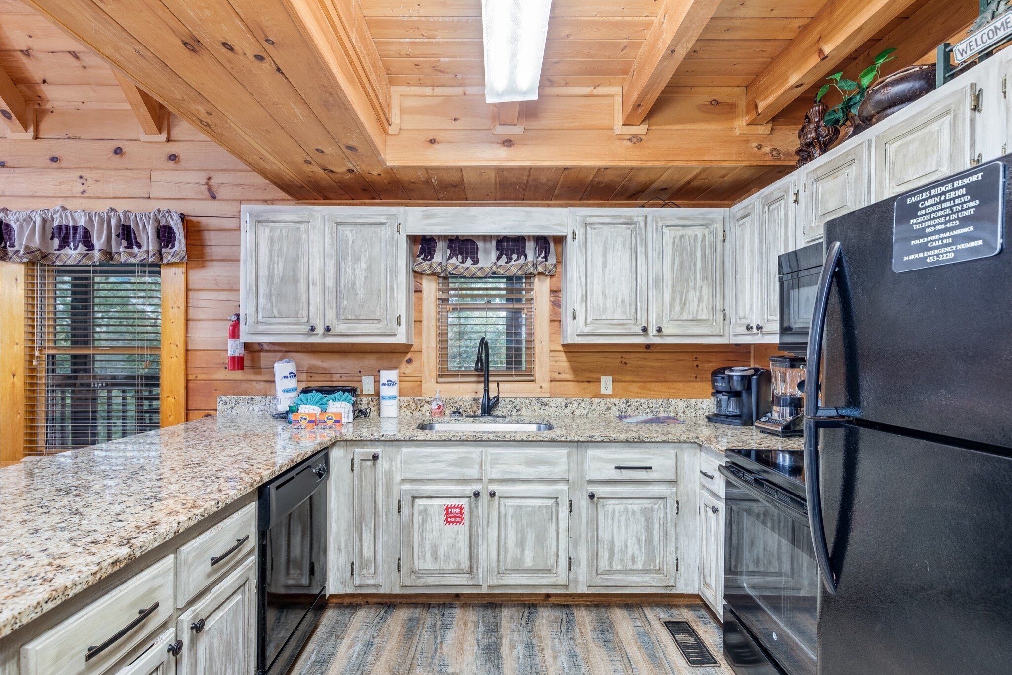 A kitchen with granite countertops, white cabinets, a black refrigerator, and a window with a decorative valance.