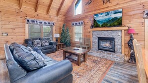 A cozy log cabin interior with a fireplace, leather sofa, and a Christmas tree. - ER101 - Heavenly Hideaway  Great location - Close to town! (Pigeon Forge)