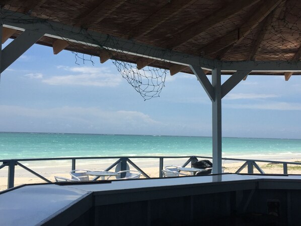 A beachside view from a covered area with a netted ceiling, overlooking the ocean.