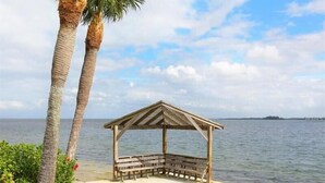 A wooden gazebo with a bench, located by a body of water.