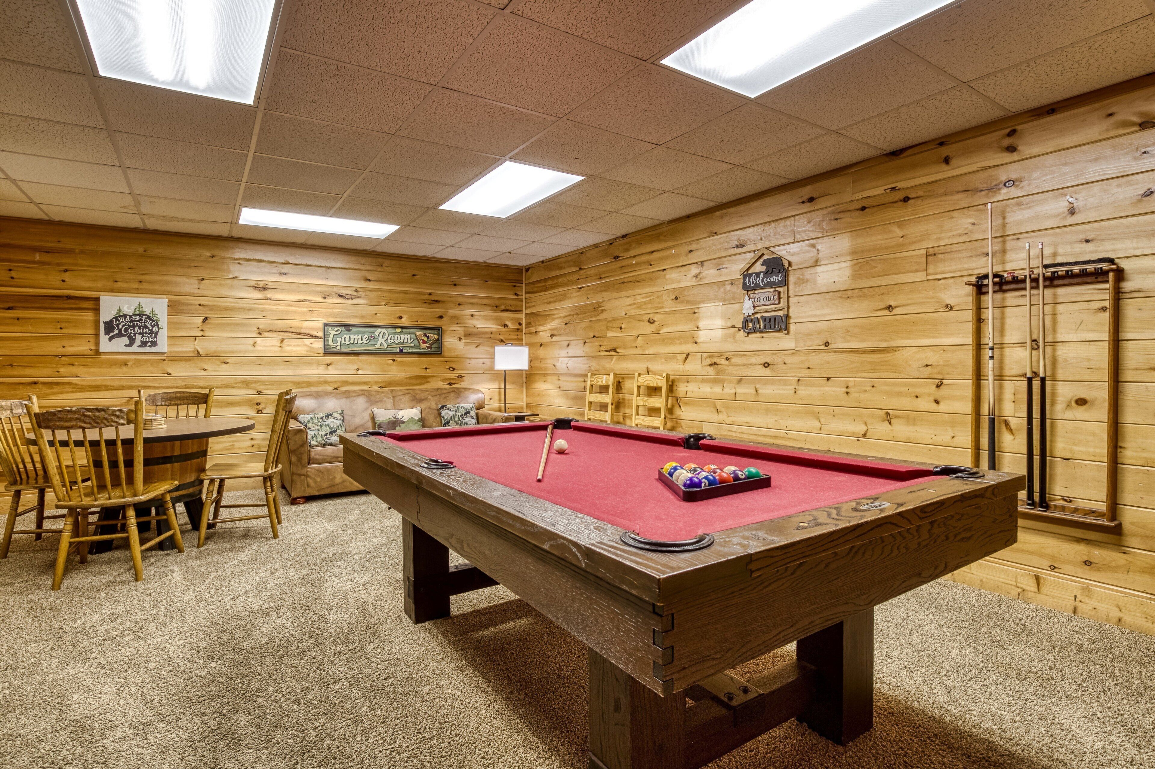 A pool table with surrounding chairs and a table, wooden walls, and a billiards rack.