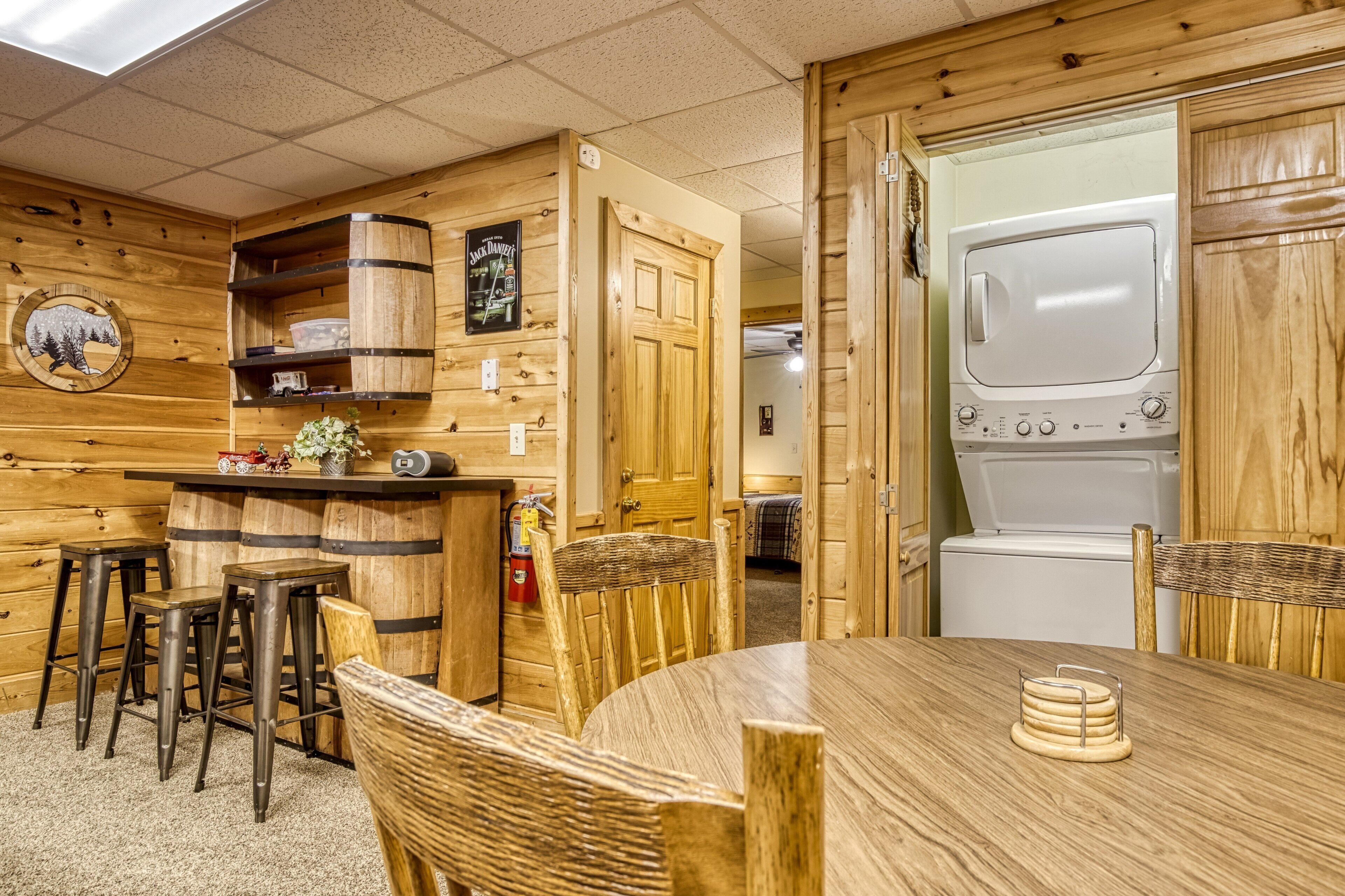 A wooden interior with a kitchen area, bar stools, a dining table, and a washing machine.