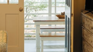 Une pièce avec un banc en bois, une porte blanche et une vue sur l’extérieur.