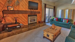 Una sala de estar acogedora con chimenea, televisor montado encima y un sofá verde con cojines de colores.