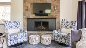 Un salon doté d’une cheminée en pierre, de deux fauteuils à motifs et d’un téléviseur fixé au-dessus de la cheminée.