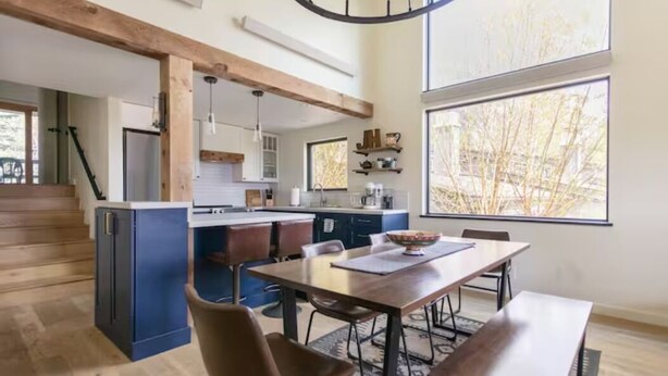 Une cuisine moderne dotée d’un îlot central, de poutres en bois et de grandes fenêtres.