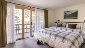 Une chambre à coucher avec un lit, une fenêtre avec des rideaux, un tableau au mur et un balcon donnant sur des arbres.