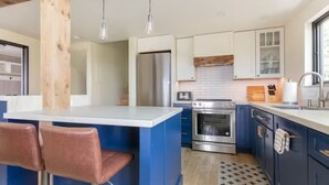 Une cuisine moderne avec des meubles bleus, un îlot central doté de tabourets, des appareils en acier inoxydable et un luminaire suspendu.
