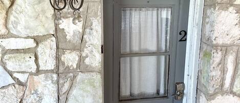 Entrada con un muro de piedra, una puerta gris, el número 2, y un candelabro de hierro forjado en la parte superior.