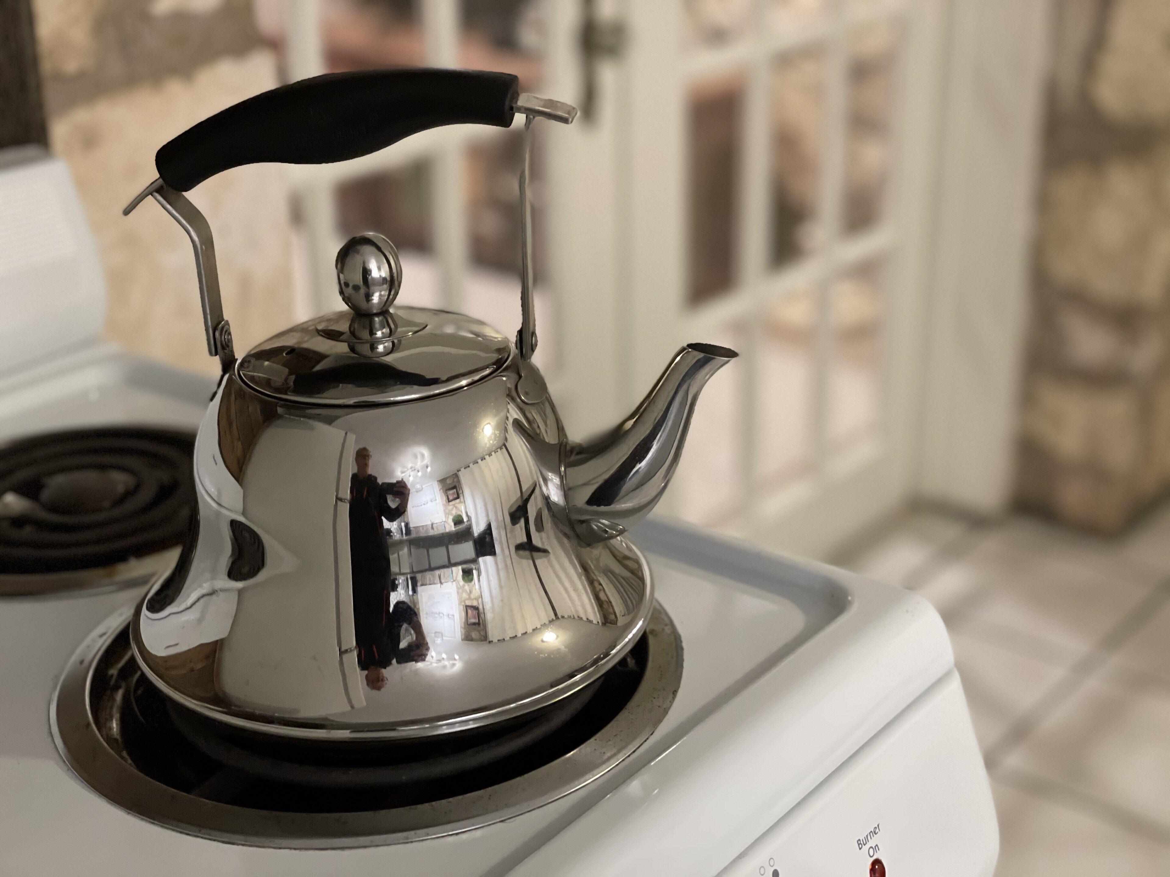 Une bouilloire en acier inoxydable posée sur une cuisinière blanche.