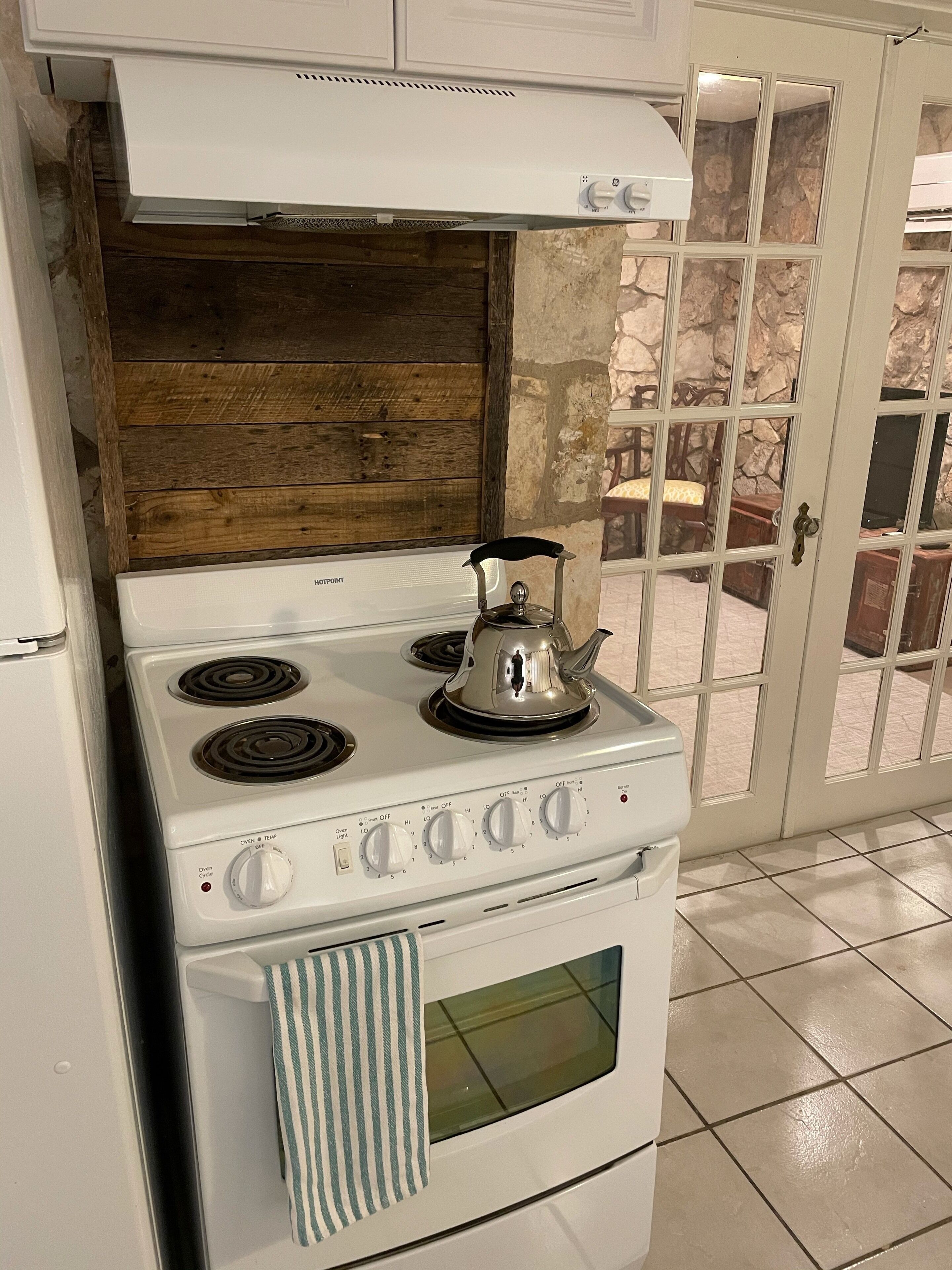 Une cuisine avec un fourneau blanc, une bouilloire et un pare-feu en bois.