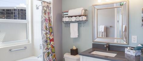 A bathroom with a bathtub, toilet, and a large mirror. There is a towel rack with towels and a tissue box.