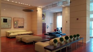 Un hall d’entrée spacieux au design moderne, comprenant un espace détente avec des canapés et des fauteuils, un comptoir d’accueil et des œuvres d’art accrochées aux murs.