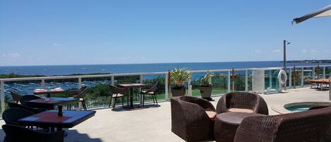A terrace with wicker furniture, a pool, and a view of the sea.